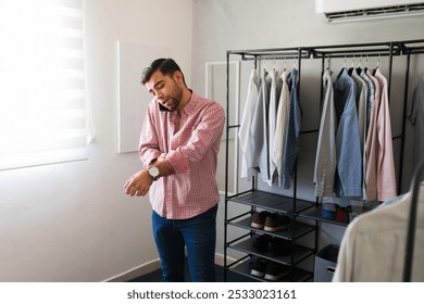 Young man multitasking, buttoning his shirt and talking on the phone while getting ready in his contemporary walk-in closet - Powered by Shutterstock