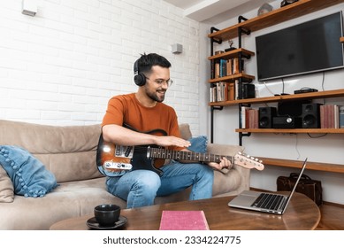 Young man music teacher giving guitar lessons to students online on laptop computer from home. Learning to play electric guitar using online course and listening melody through wireless headphones. - Powered by Shutterstock