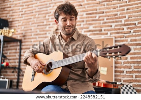 Young man musician smiling confident playing classical guitar at music studio
