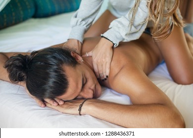 young man with a naked torso lying on the bed. A beautiful girl is sitting on hin and doing to him a back massage.