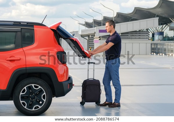 Young man near car with luggage closes tailgate\
in parking.