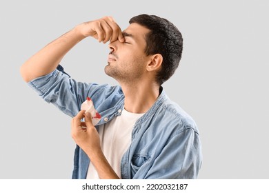 Young Man With Nosebleed And Tissue On Light Background