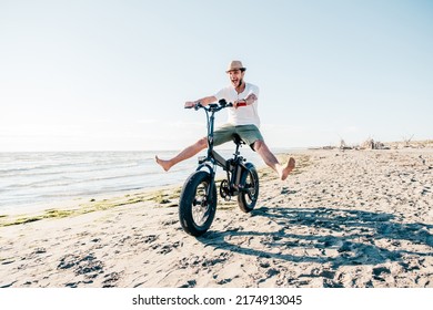 Young Man On Bicycle Having Fun With Electric Bike - Carefree Boy Having Fun And Smiling On Bicycle On The Beach On A Sunny Day - Freedom Concept