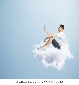 Young man on cloud using smartphone. Dream and communication concept 