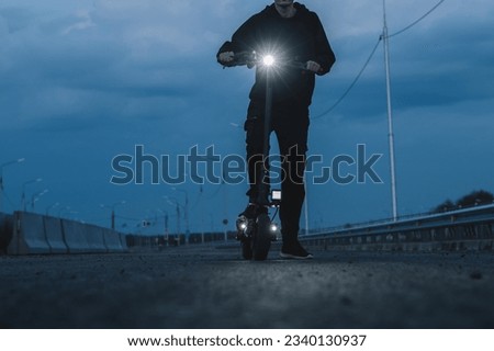 Young man on an electric scooter at night on an empty road. Light from a flashlight.