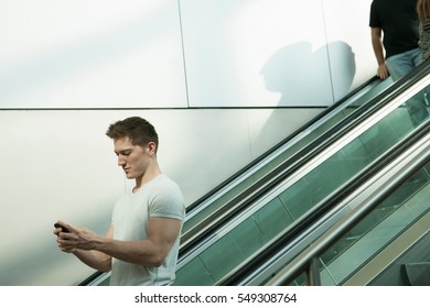 Young man on escalator using smartphone