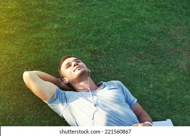 young man on the grass listening music on tablet