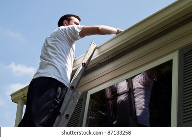 Young Man On Latter Cleaning House Gutters