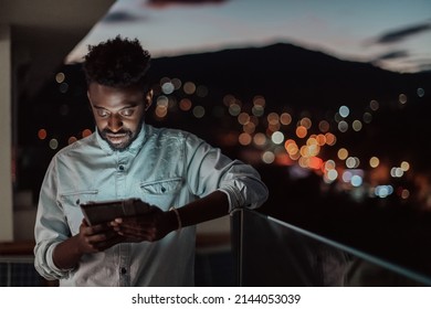 The young man on an urban city street at night texting on smartphone with bokeh and neon city lights in the background. 
