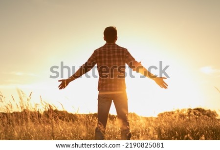 Young man in an open field looking up feeling energized by the warm rays of sunshine lifting arms up to the sunset sky. Letting go of your fears concept Foto stock © 