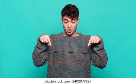 young man with open mouth pointing downwards with both hands, looking shocked, amazed and surprised
