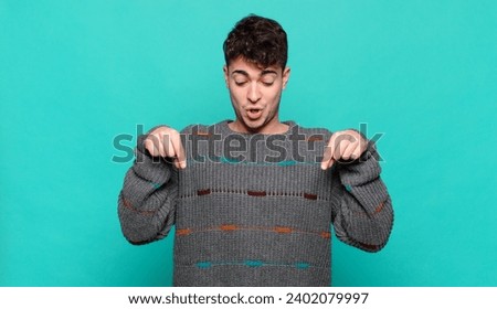 young man with open mouth pointing downwards with both hands, looking shocked, amazed and surprised