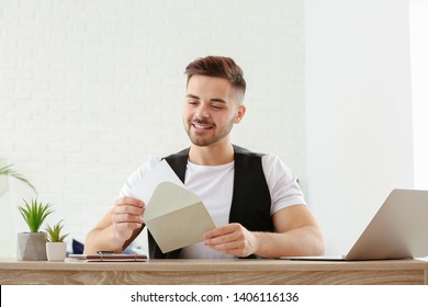 Young Man Opening Envelope With Invitation At Home