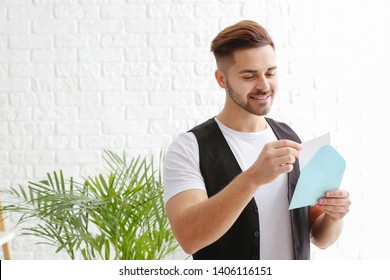 Young Man Opening Envelope With Invitation At Home