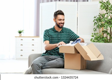 Young Man Opening Parcel On Sofa At Home