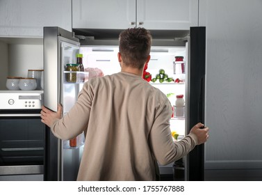 Young Man Opening Refrigerator Indoors, Back View