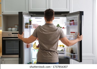 Young Man Opening Refrigerator In Kitchen, Back View