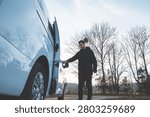 Young man opens a white van door on a rural roadside, photographed from a low angle in warm late-autumn sunlight before a road trip under a clear sky