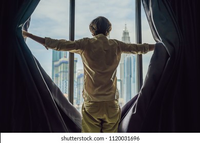 Young man opens the window curtains and looks at the skyscrapers in the big city. - Powered by Shutterstock