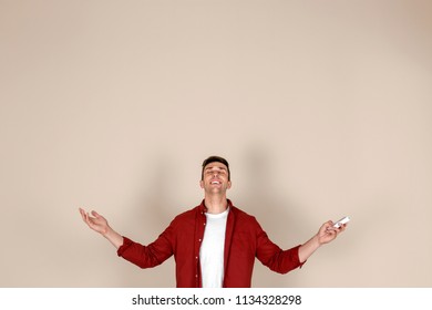 Young Man Operating Air Conditioner With Remote Control On Light Background