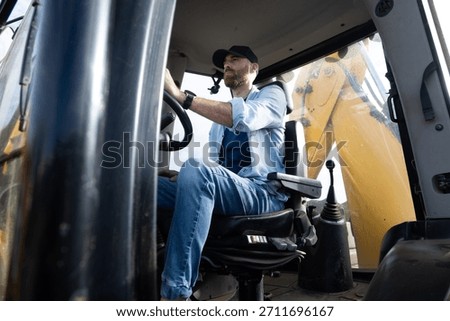 Young man operating a backhoe loader in the countryside