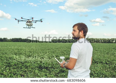Young man operating of flying drone octocopter at the green field. Professional agriculture drone flying with blue sky.
