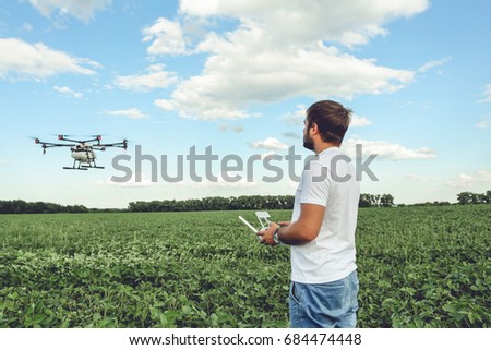 Young man operating of flying drone octocopter at the green field. Professional agriculture drone flying with blue sky.