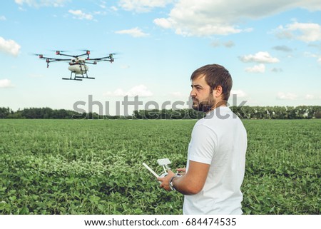 Young man operating of flying drone octocopter at the green field. Professional agriculture drone flying with blue sky.