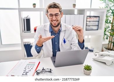 Young Man Optician Holding Glasses Using Laptop At Clinic