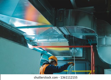 Young Man In Orange Work Vest, Safety Belt And Hard Hat Going To Repair HVAC System. Toned Photography.