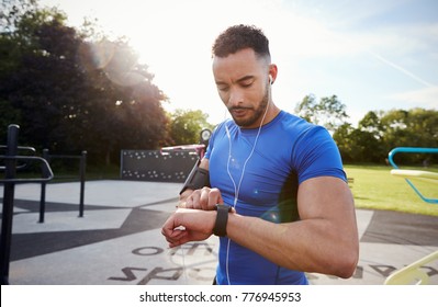 Young man at outdoor gym setting fitness app on smartwatch