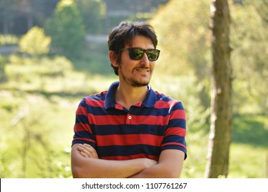 Young Man Outdoors Portrait Not Looking At The Camera With Natural Green Background. Happy Facial Emotion.