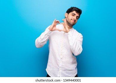 Young Man Over Isolated Blue Wall Making Heart Symbol By Hands