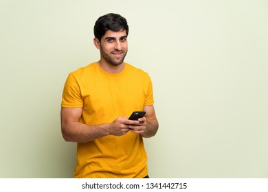 Young Man Over Pink Wall Sending A Message With The Mobile