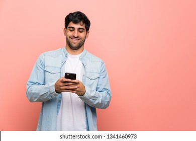 Young Man Over Pink Wall Sending A Message With The Mobile