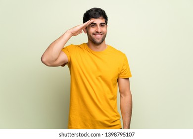 Young man over pink wall saluting with hand