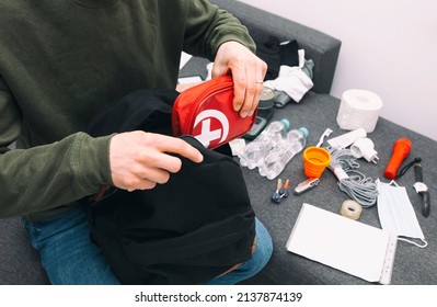 Young man packing the bag with documents, water,food, first aid kit and other items needed to survive