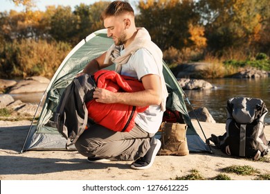 Young Man Packing Sleeping Bag Near Camping Tent Outdoors