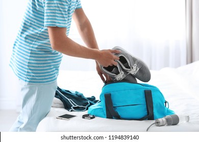 Young Man Packing Sports Stuff For Training Into Bag In Bedroom