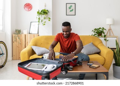 Young Man Packing Travel Bag For Summer Vacation - African Male Preparing Suitcase Before Going On Holidays