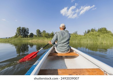 Young man paddling a canoe during a vacation on the mountain lake, enjoying pleasant summer sun rays. Nature getaway concepts. - Powered by Shutterstock