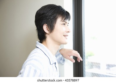 Young Man In Pajama Standing Beside The Window And Looking At Outside