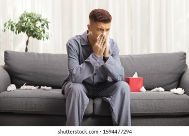 Young Man In Pajamas Blowing His Nose At Home On The Couch 