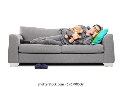 Young Man In Pajamas Sleeping On Couch With Teddy Bear Isolated On White Background