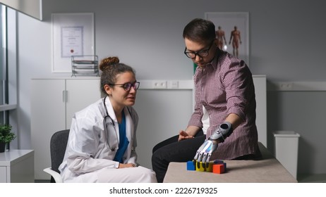 Young man patient with bionic arm build tower with wooden blocks at rehabilitation center. Man with hand prosthesis visit doctor for rehabilitation exercises - Shutterstock ID 2226719325