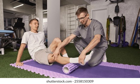 Young man, patient sitting on foam roller with physiotherapist guiding the movement for muscle recovery and rehabilitation exercises. Concept of rehabilitation, recovery, healthcare, physical therapy - Powered by Shutterstock