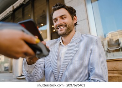 Young man paying cellphone in cafe while waitress holding payment terminal - Powered by Shutterstock