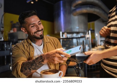 A young man pays with his smartphone with a smile after drinking coffee in a local - Powered by Shutterstock