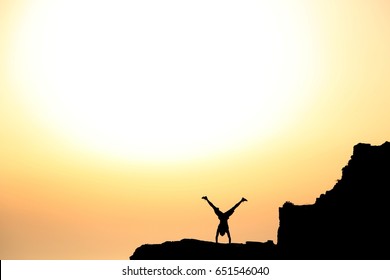 A young man is performing a handstand at a cliff in croatia. In the background the sun is going down. The man is only visible by his silhouette. The photo was taken at a cliff in croatia in june 2014.