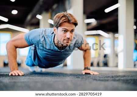 Young man performing pushup exercise on gym floor, focusing on strength, training, and a healthy lifestyle